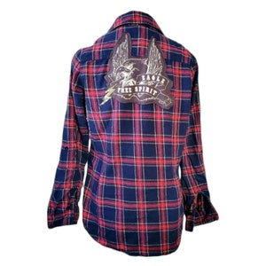 May include: A blue and red plaid long-sleeved shirt with a brown patch on the back that says "Eagle Free Spirit" with a drawing of an eagle with wings spread.