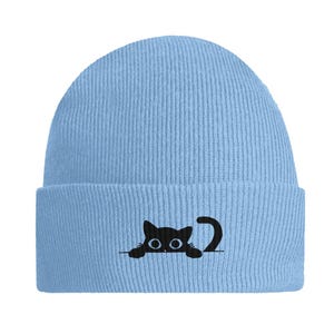 Könnte beinhalten: Eine hellblaue Mütze mit einer schwarzen gestickten Katze, die hinter einer weißen Linie hervorguckt. Die Katze hat große Augen und einen Schwanz.