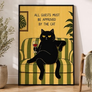 Könnte beinhalten: Ein gerahmter Kunstdruck mit einer schwarzen Katze, die auf einem gelb-grün gestreiften Sofa sitzt und ein Glas Rotwein hält. Der Text über der Katze lautet, ALL GUESTS MUST BE APPROVED BY THE CAT. Ein kleines gerahmtes Bild eines Blattes hängt an der Wand.