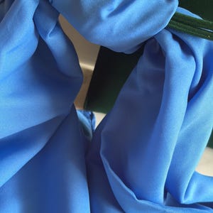 Peut inclure: Gros plan sur un foulard bleu clair avec un motif noué. Le foulard est fait d'un tissu lisse et soyeux. Un objet vert foncé est partiellement visible en arrière-plan.