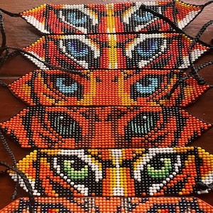 May include: Six woven beaded bracelets featuring tiger eye patterns in various colours including orange, black, white, blue, and green. Each bracelet has a pointed end and black braided cord ties for adjustable closure, displaying detailed beadwork.
