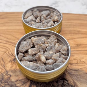 Two small tins filled with Sumatra Benzoin resin tears placed on a wooden surface.