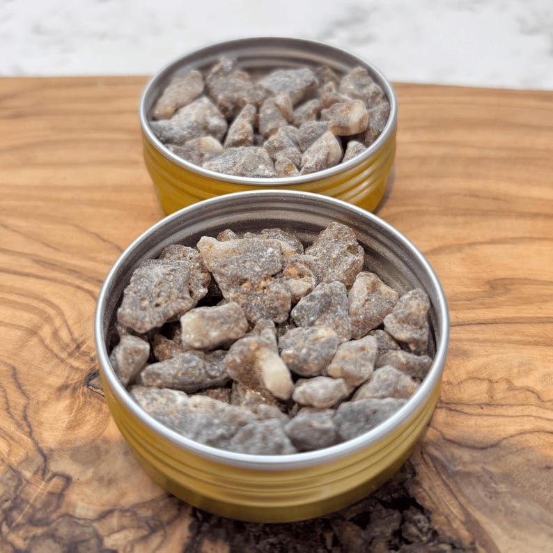 Two small tins filled with Sumatra Benzoin resin tears placed on a wooden surface.