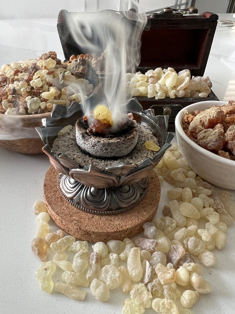 A display of burning copal resin on a charcoal disc in a decorative metal incense holder, producing thick aromatic smoke.