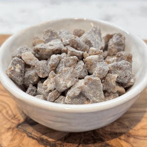 A small ceramic bowl filled with Sumatra Benzoin resin tears, showcasing rough, grayish-brown pieces with a natural, rugged texture.