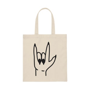Peut inclure: Un sac fourre-tout beige avec un dessin au trait noir d'une main faisant le geste de la langue des signes "Je t'aime".