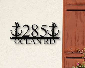 May include: A black metal house number sign featuring the digits 285 flanked by two anchor icons on the sides. Below the numbers, the text OCEAN RD is displayed in a bold, capitalized font. The sign has mounting holes on each end.