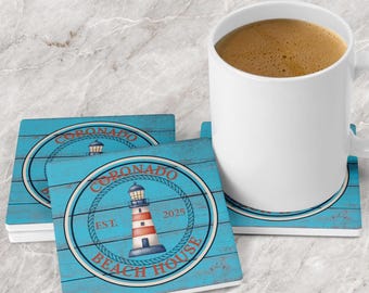 May include: A white ceramic mug and two square coasters featuring a blue wood-plank background. Each coaster displays a circular emblem with a rope border, a red and white lighthouse illustration, and the text CORONADO BEACH HOUSE EST. 2025.