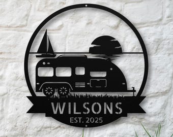 May include: A circular black metal wall sign featuring a silhouette of a travel trailer, a sailboat, and a sunset. A banner at the bottom displays the text "WILSONS" in large capital letters and "EST. 2025" in smaller text below the name.