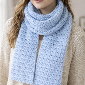 May include: A light blue, knitted scarf. The scarf is wrapped around the neck and drapes down the front. The scarf is made of a soft, textured yarn. The scarf is a solid color and has a simple, classic design. The scarf is a cozy accessory.