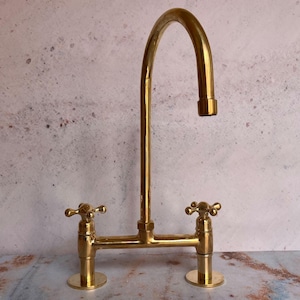 May include: A gold-toned kitchen faucet with two handles and a high spout. The faucet has a traditional design with cross-shaped handles.