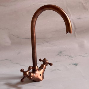 May include: A copper kitchen faucet with a high arc spout and cross-shaped handles.