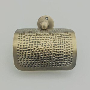May include: A hammered brass toilet paper holder with a round base. The holder has a textured surface and a simple design.