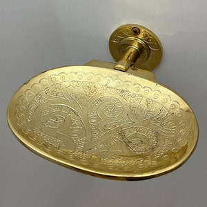 Pode incluir: Um saboneteira de latão dourado com um design floral ornamentado. A saboneteira está presa a um suporte de parede com um rolo decorativo.