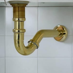 Op de afbeelding: Een gouden P-vormige sifon met een schroefdraad en een wandbevestiging.