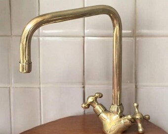 May include: A polished brass kitchen faucet with a high arc spout and two cross-shaped handles.