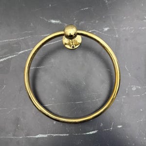 May include: A gold-toned metal towel ring with a round base and a smooth, circular ring.