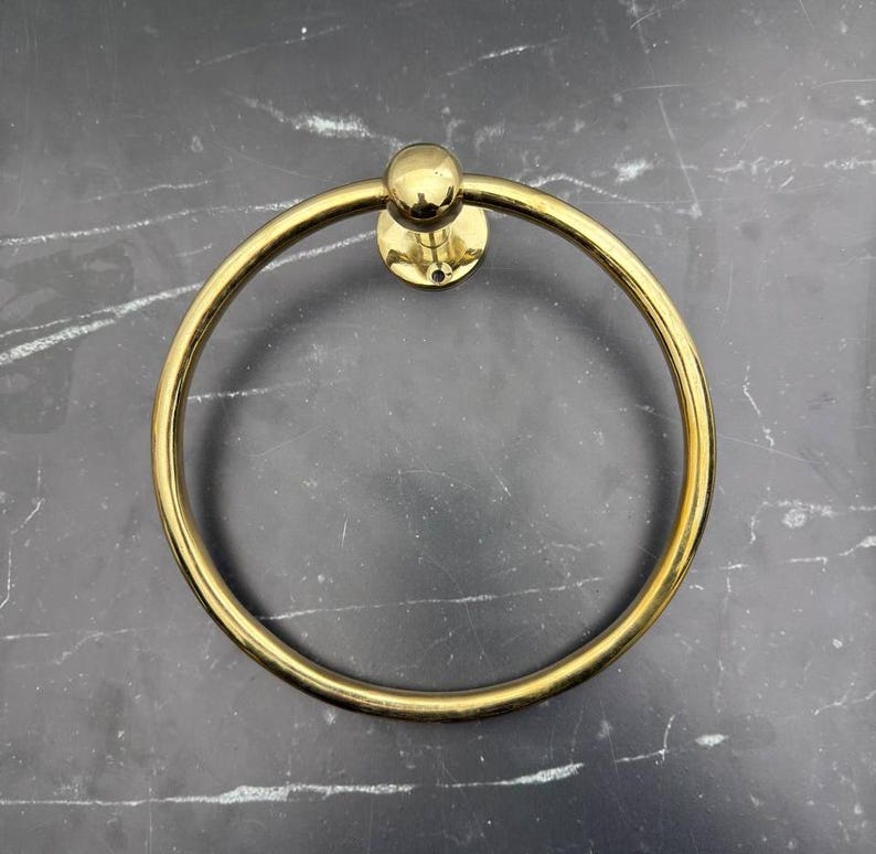 May include: A gold-toned metal towel ring with a round base and a smooth, circular ring.