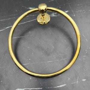 May include: A gold-toned metal towel ring with a round base and a smooth, circular design.
