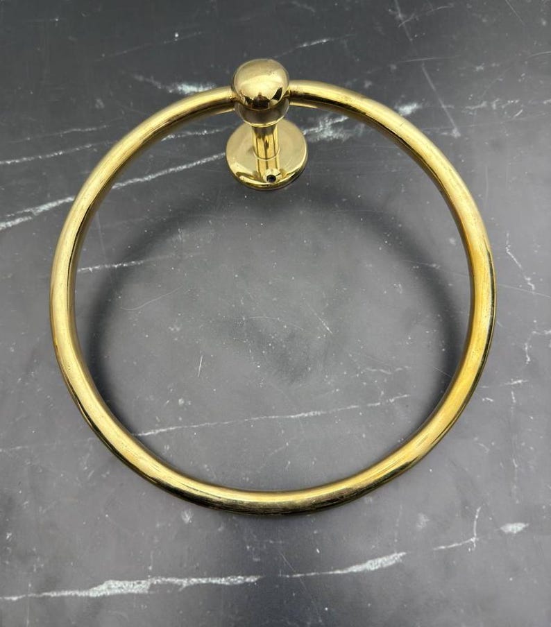 May include: A gold-toned metal towel ring with a round base and a smooth, circular design.