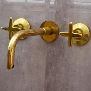 K&ouml;nnte beinhalten: Ein goldfarbener Badezimmerhahn mit zwei kreuzf&ouml;rmigen Griffen.