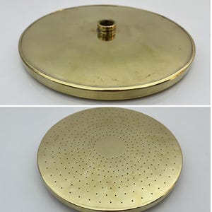 Peut inclure: Une pomme de douche de couleur dorée avec un design circulaire et un trou central. La pomme de douche a un motif de petits trous autour du bord et au centre.