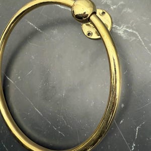 May include: A gold-toned metal towel ring with a round base and a smooth, circular design.