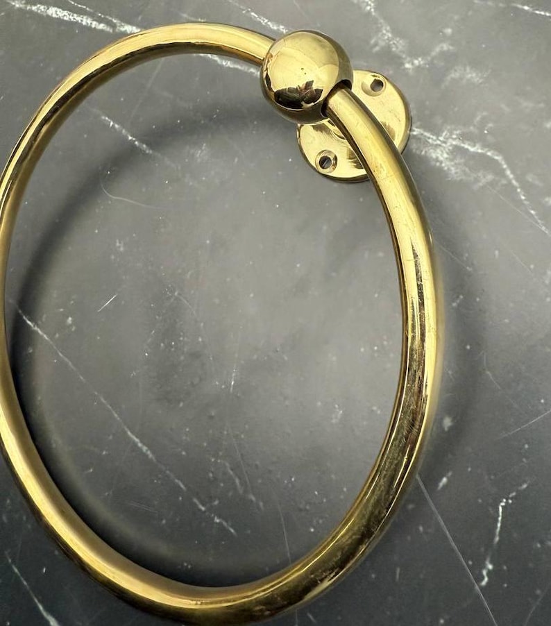 May include: A gold-toned metal towel ring with a round base and a smooth, circular design.