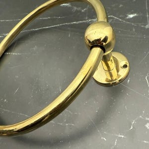 May include: A gold-toned metal towel ring with a round base and a smooth, polished finish.