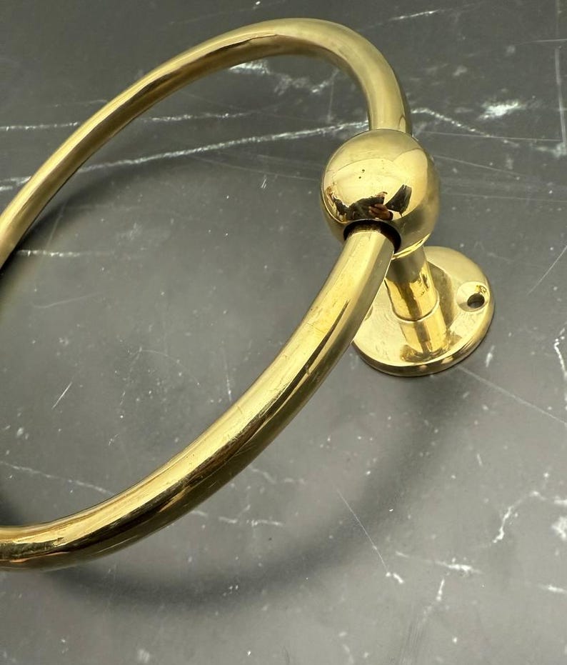May include: A gold-toned metal towel ring with a round base and a smooth, polished finish.