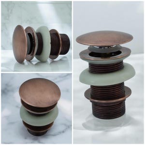 Peut inclure: Gros plan sur un bouchon de lavabo de salle de bain de couleur cuivre. Le bouchon a un dessus rond et une série d'anneaux concentriques. Le bouchon est présenté dans trois positions différentes.