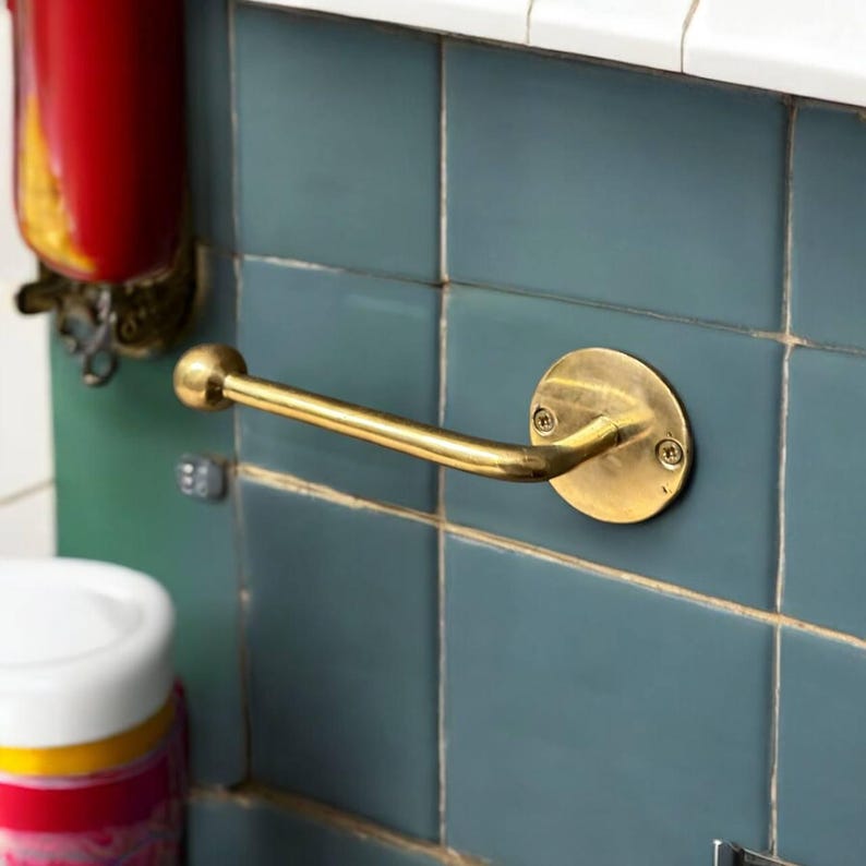 Puede incluir: Un porta rollo de papel higi&eacute;nico de lat&oacute;n montado en una pared de azulejos azules. El soporte tiene una base redonda y un brazo curvo.
