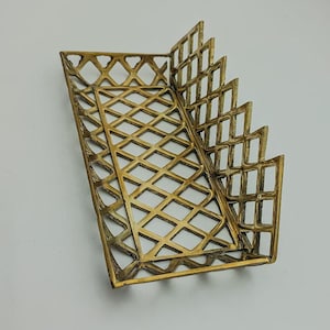 May include: A gold-toned metal tray with a geometric diamond pattern. The tray has a rectangular shape with a raised edge and a decorative, scalloped design on the side.
