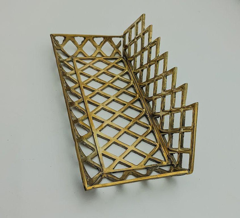 May include: A gold-toned metal tray with a geometric diamond pattern. The tray has a rectangular shape with a raised edge and a decorative, scalloped design on the side.