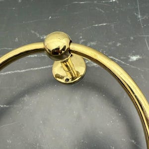 May include: A gold-toned metal towel ring with a round base and a smooth, rounded edge. The ring is designed to hold towels or other items.