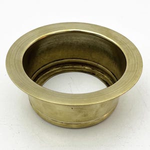 May include: A gold-colored metal drain ring with a smooth, rounded edge. The ring has a slightly raised lip around the outer edge.