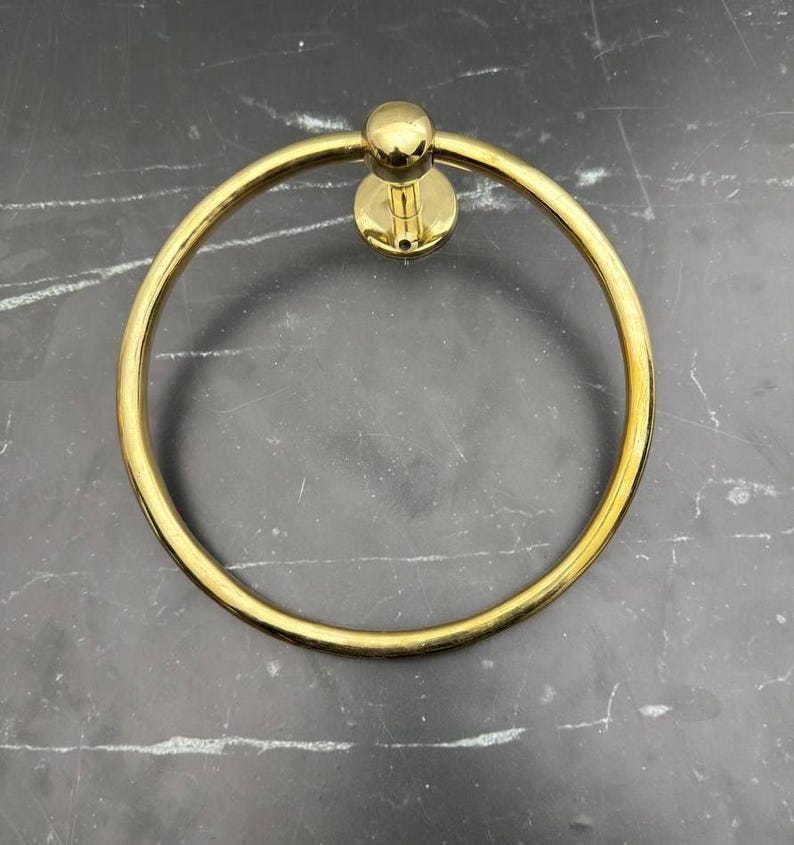 May include: A gold-toned metal towel ring with a round base. The ring is smooth and shiny.