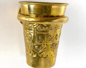 May include: A gold metal cup with an intricate design is attached to a wall mount. The cup has a decorative pattern and a smooth, shiny finish.