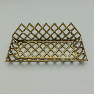 May include: A gold metal tray with a diamond-shaped grid pattern. The tray is rectangular and has a raised edge.