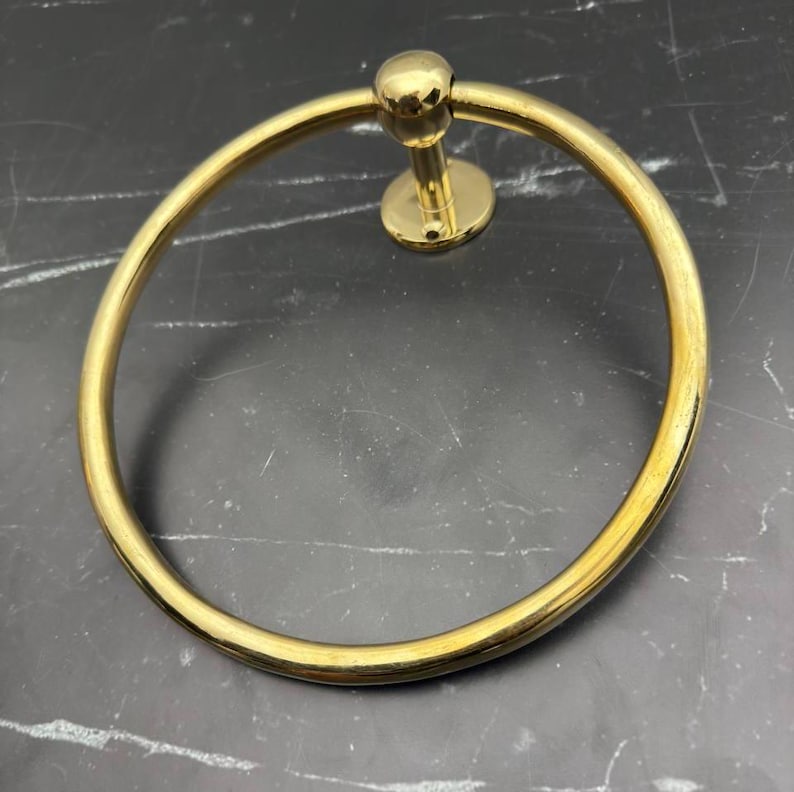 May include: Gold-toned metal towel ring with a round base and a smooth, circular ring.