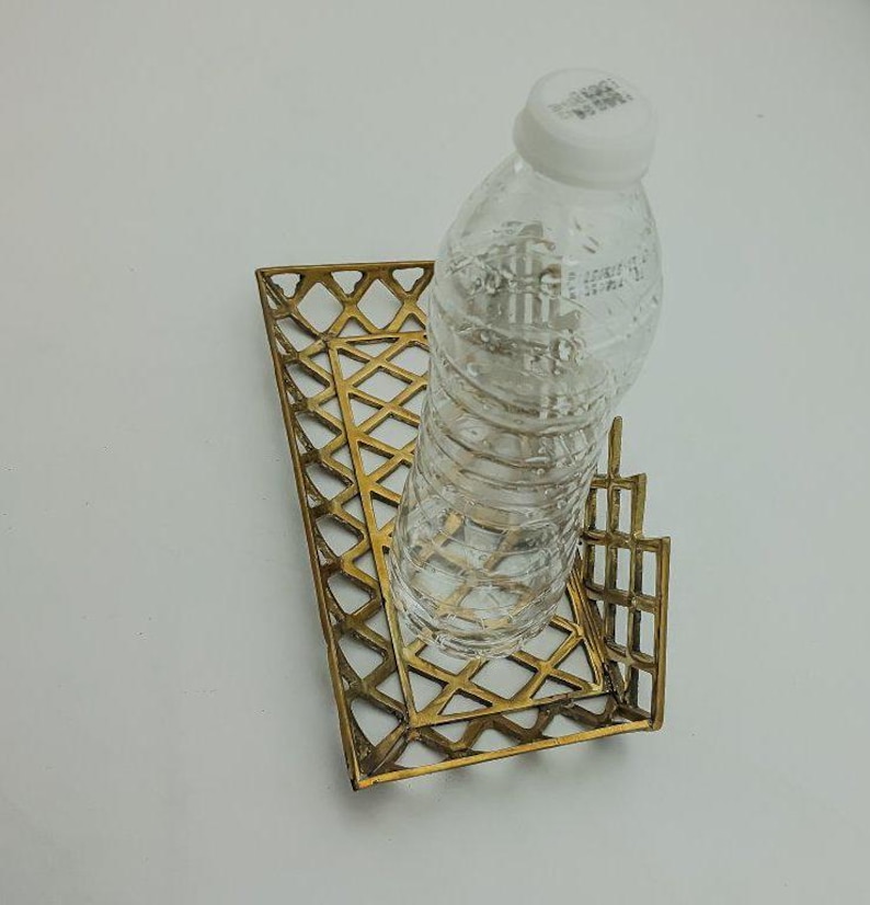 May include: A gold metal tray with a geometric design holds a clear plastic water bottle.