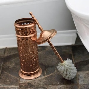 Peut inclure: Une brosse de toilette et un porte-brosse en cuivre avec un motif en relief complexe. La brosse a une tête de poils blancs et un manche en cuivre.