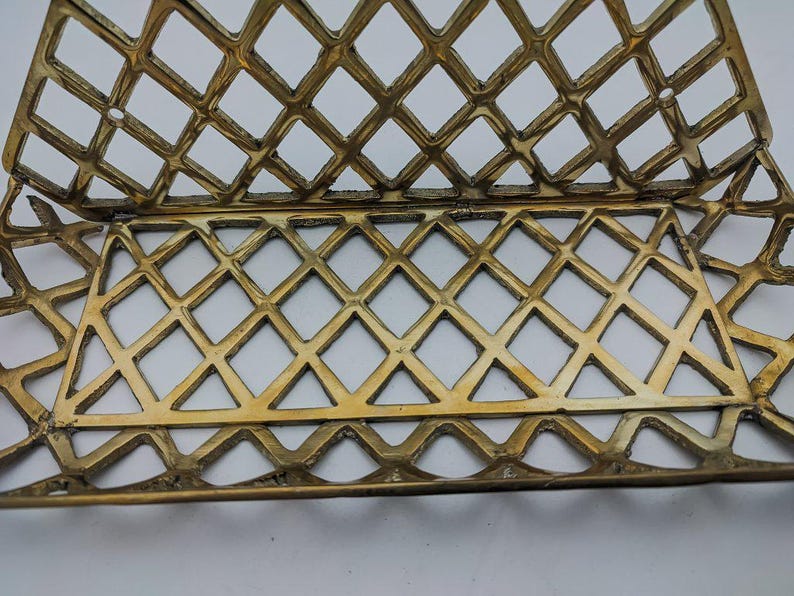 May include: A gold-colored metal letter holder with a diamond-shaped grid pattern. The holder is designed to hold letters or other documents.