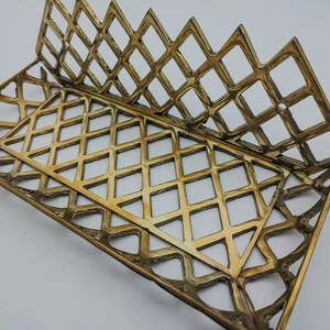 May include: A gold metal decorative stand with a diamond-shaped grid pattern. The stand is designed to hold items like books or magazines.