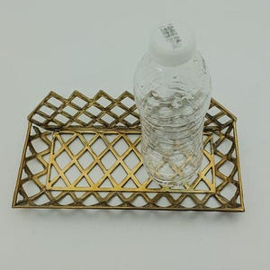 May include: A gold metal tray with a diamond pattern design. A clear plastic water bottle is sitting on the tray.