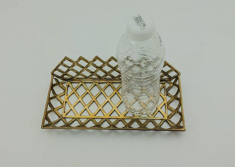 May include: A gold metal tray with a diamond pattern design. A clear plastic water bottle is sitting on the tray.