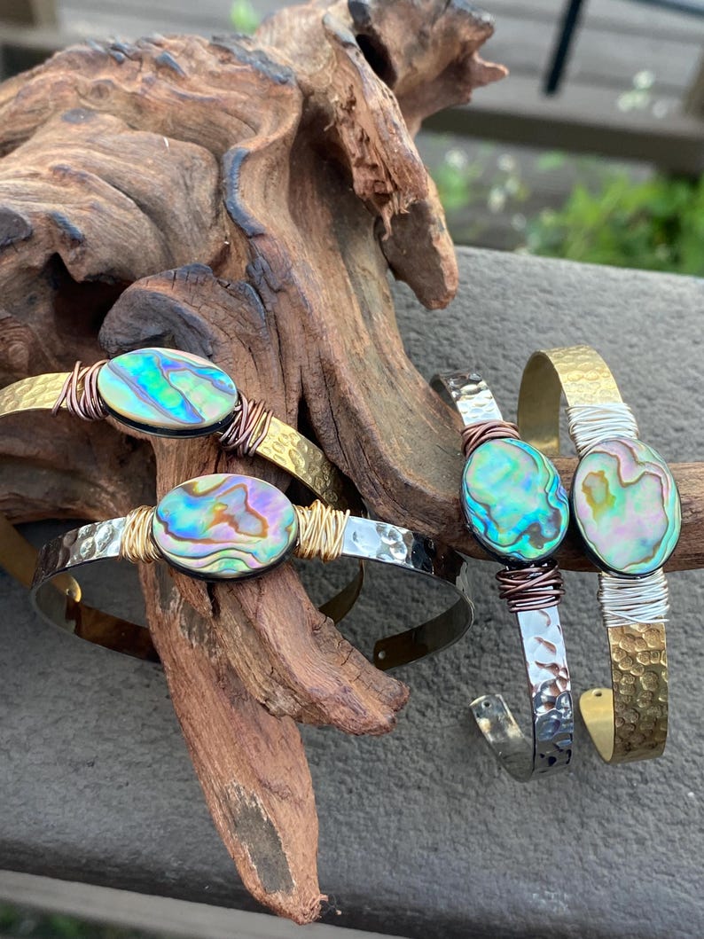 May include: Three bracelets with abalone shell accents. The bracelets are made of hammered metal with copper wire accents. The abalone shells are iridescent with shades of green, blue, and purple.