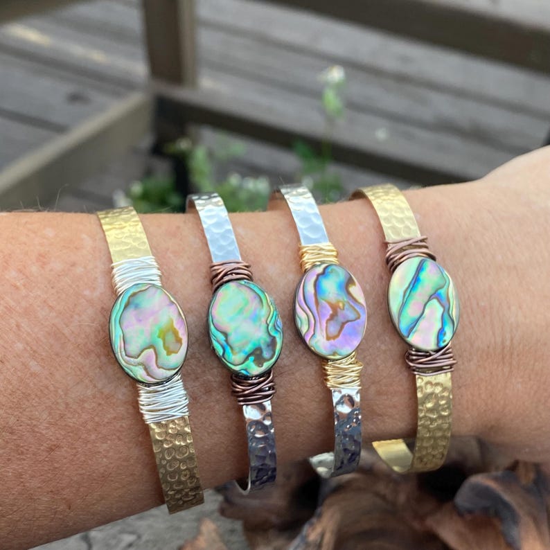 May include: Four hammered metal bracelets with abalone shell accents. The bracelets are in gold, silver, and copper tones.