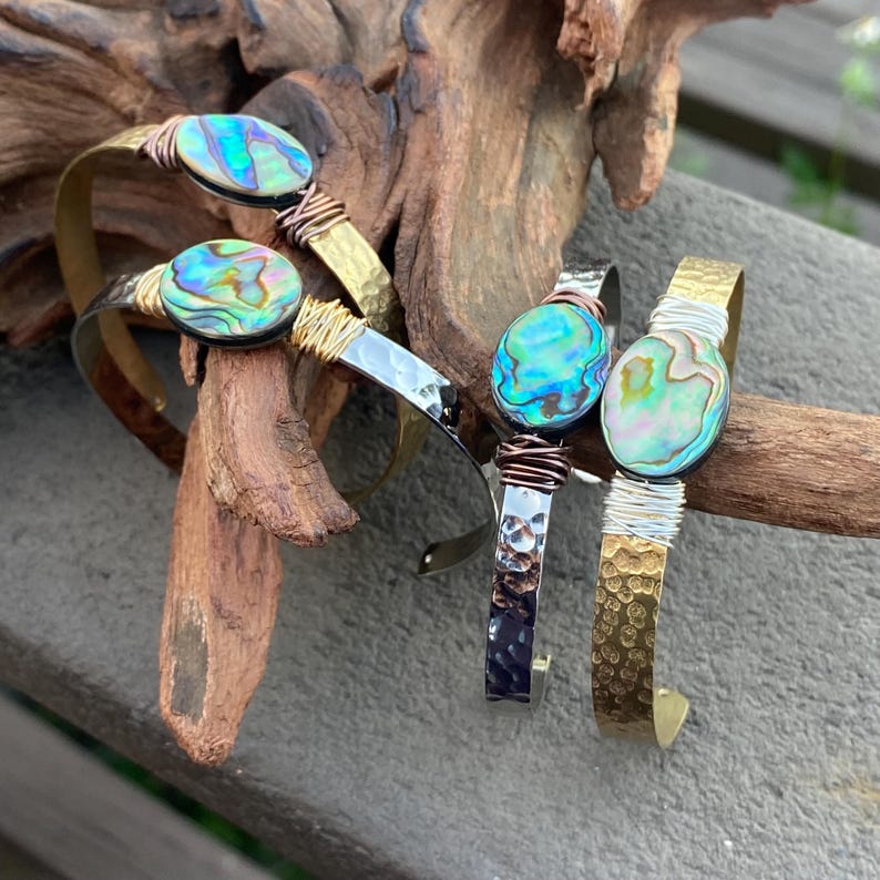 May include: Three bracelets with hammered metal bands and abalone shell accents. The bracelets are in gold, silver, and copper tones.