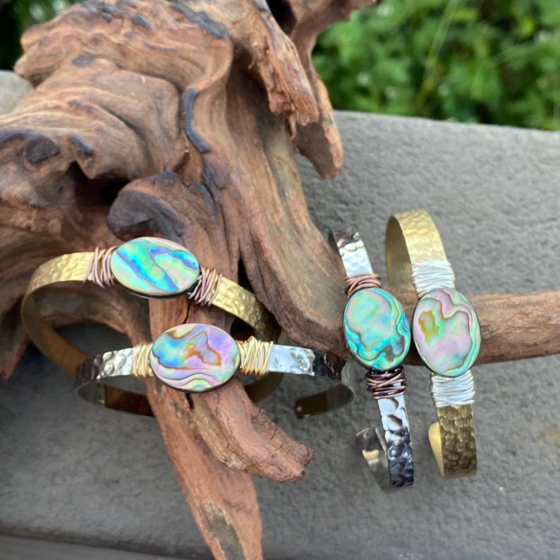 May include: Three bracelets with abalone shell accents. The bracelets are made of hammered metal with copper wire accents. The abalone shells are iridescent with shades of green, blue, and purple.